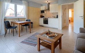 Eine moderne Küche mit weißen Schränken, einer Mikrowelle und einem Backofen. Ein Essbereich mit Holztisch und Stühlen, sowie ein kleiner Holztisch mit einer Serviertafel mit Essen.