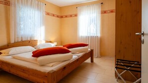 A double bed with white and red pillows, wooden headboard, and a wooden door.