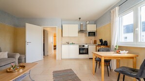 A modern kitchen with white cabinets, a dining table with chairs, a sofa, and a large window.