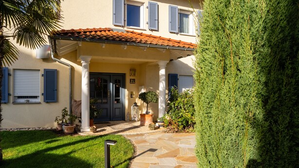 A building with a stone pathway leading to a dark door, potted plants, and a well-maintained lawn. - Apartment 'Fewo Cannobio' with Balcony and Wi-Fi (Gengenbach)