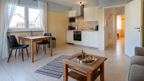 A modern kitchen with white cabinets, a microwave, and an oven. There is a dining area with a wooden table and chairs, and a small wooden table with a tray of food. - Apartment 'Fewo Cannobio' with Balcony and Wi-Fi (Gengenbach)