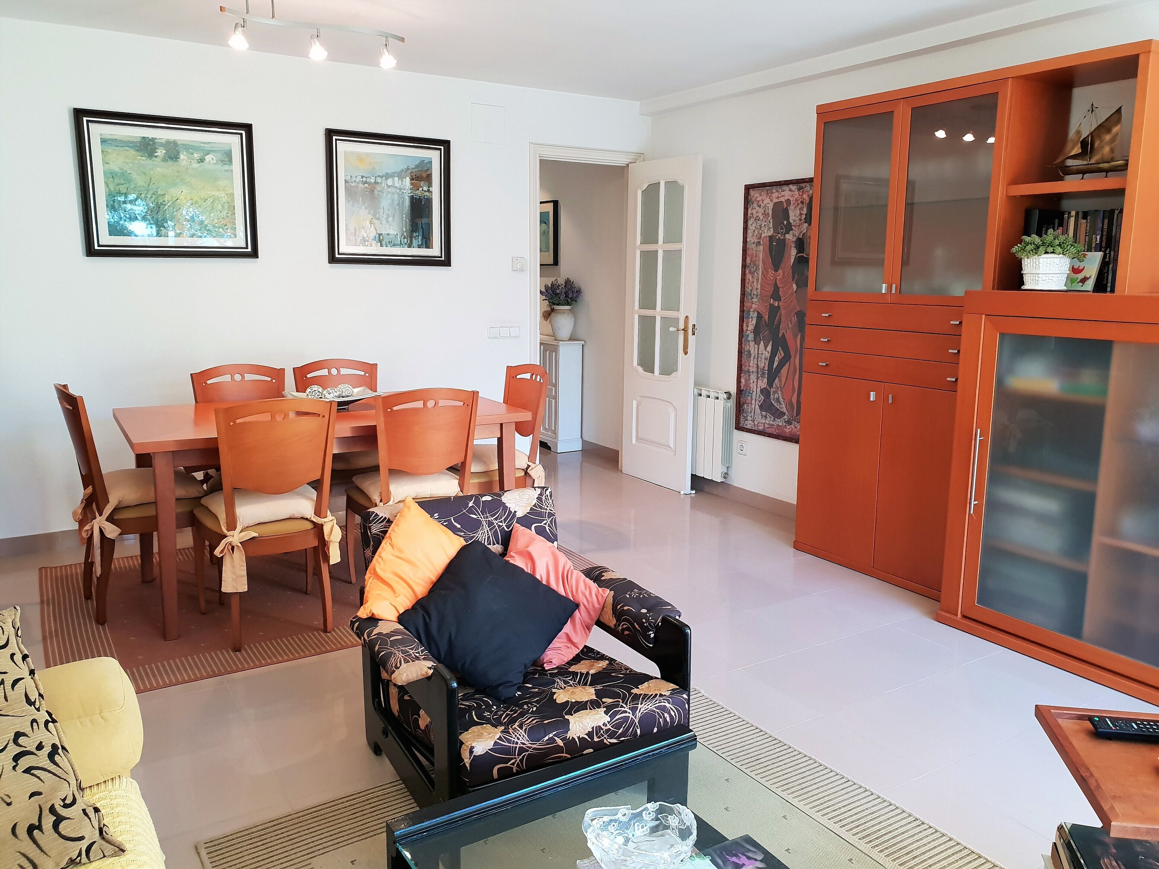 A living room with a sofa, a dining table with chairs, a cabinet, and two framed pictures on the wall.