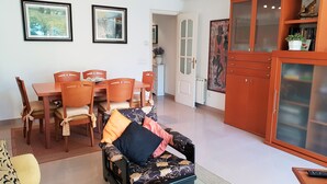 Ein Wohnzimmer mit einer Couch, einem Esstisch mit Stühlen, einem Schrank und zwei gerahmten Bildern an der Wand.