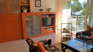 Ein Wohnzimmer mit einer Couch, einem Glastisch, einem Fernseher und einer Vitrine.