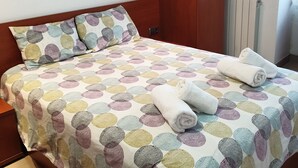Ein ordentlich gemachtes Bett mit farbenfroher Punkte-Bettdecke, zwei Kissen und gerollten Handtüchern.