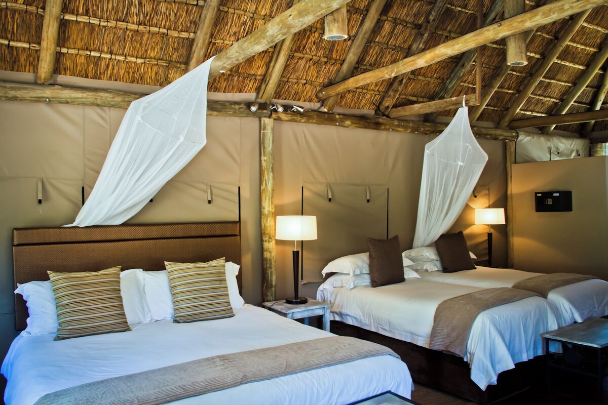 A hotel room with two beds, each with a canopy, a bedside table, a lamp, and a wall-mounted control panel.