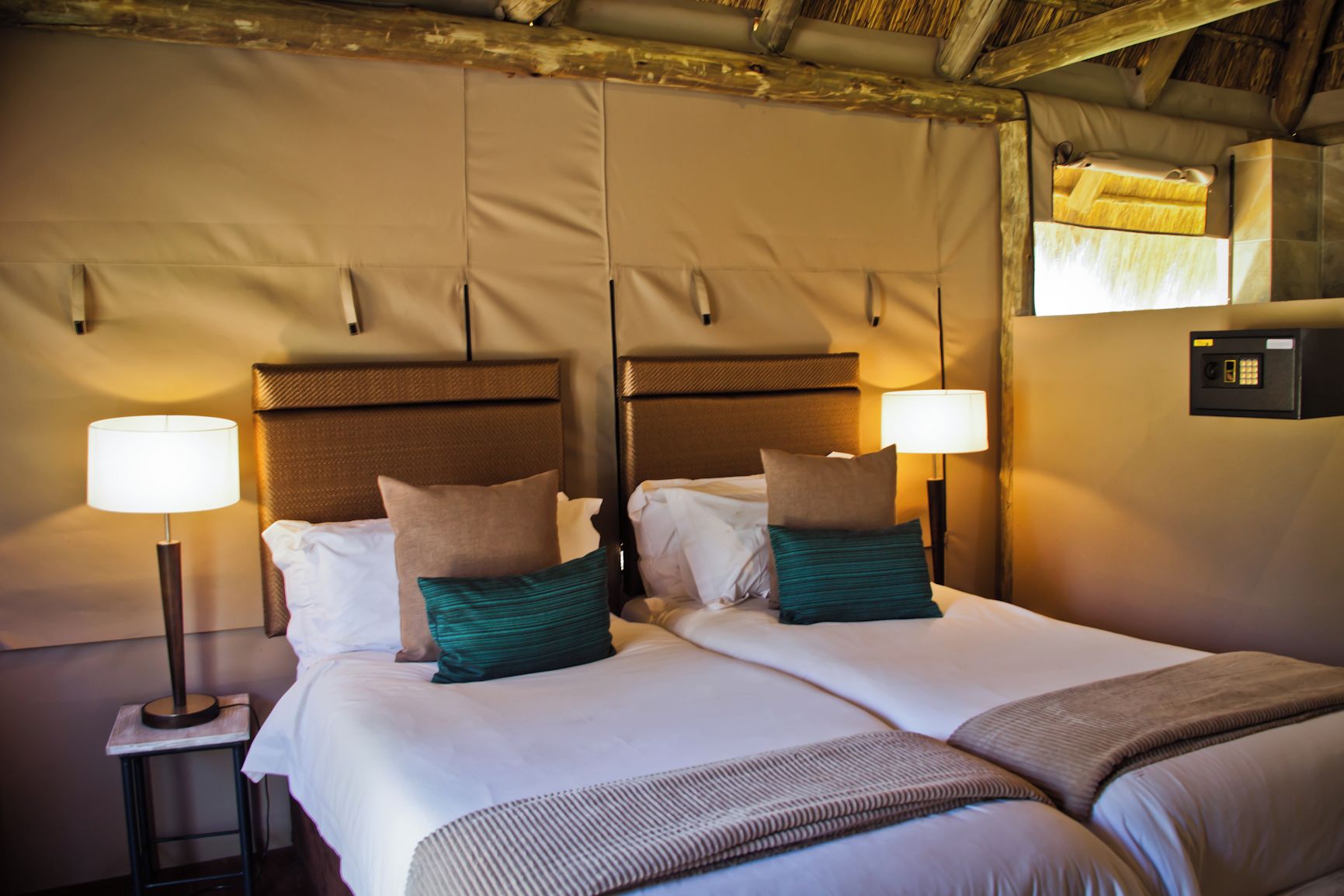 Uma cama de casal com duas mesas de cabeceira, cada uma com uma luminária, em quarto com teto de madeira e painel de controle fixado na parede.