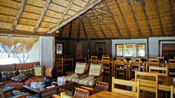 A spacious room with a high thatched ceiling, wooden furniture, and a large window providing natural light.