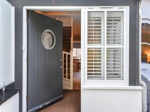 A gray door with a round window, a white window with shutters, and a staircase leading to an interior space. - 3 bedroom accommodation in Salcombe (Salcombe)