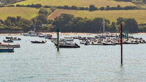 Una marina con imbarcazioni ormeggiate, una spiaggia sabbiosa e un paesaggio collinare sullo sfondo.