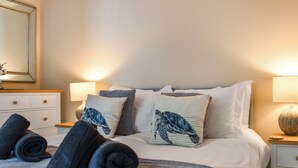 Un letto rifatto con cura, con una coperta a fantasia, due cuscini con un motivo a tartaruga e asciugamani arrotolati sul letto.