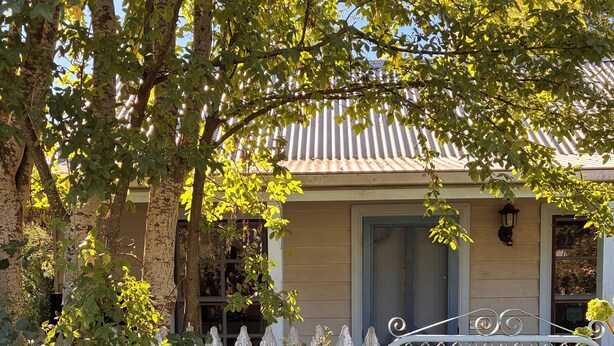 Une maison avec une clôture en bois, un portail en métal et un arbre aux feuilles vertes.