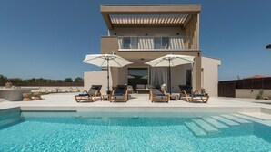 A modern two-story building with a swimming pool in front. There are lounge chairs and umbrellas around the pool area. - Villa Luna d'oro (Zakynthos)