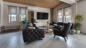 A modern living room with a large flat-screen TV, two sofas, a coffee table, and a bench. - Villa Luna d'oro (Zakynthos)