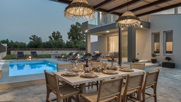 An outdoor dining area with a pool, wicker chairs, and a table set for a meal. - Villa Luna d'oro (Zakynthos)