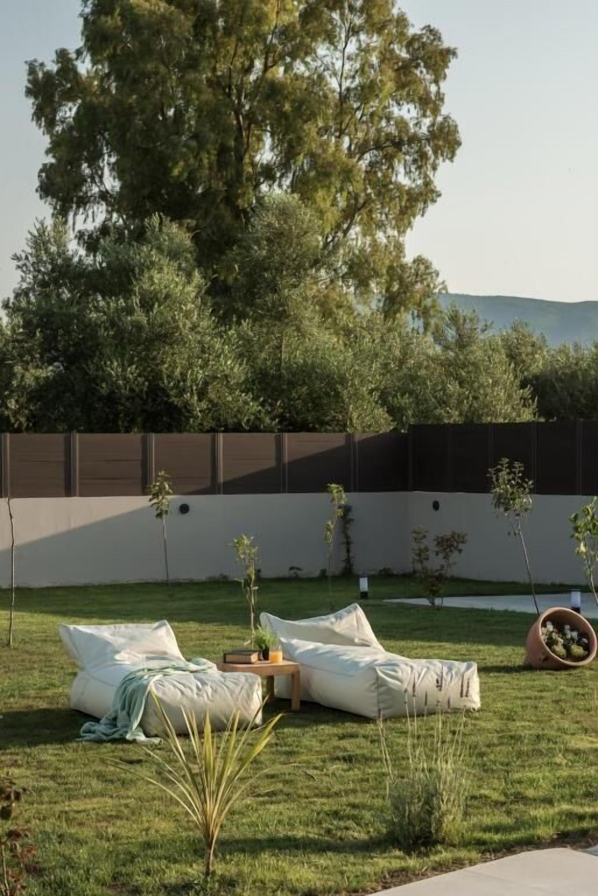 An outdoor seating area with cushions and a small table, surrounded by grass and trees.