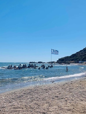 Ein Strand mit einer Flagge, Kieselsteinen und klarem Wasser.
