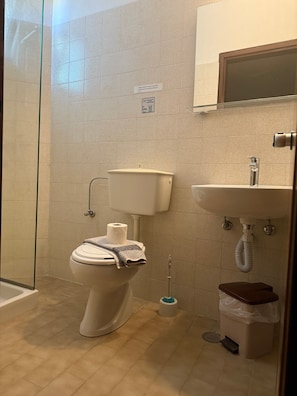 Ein Badezimmer mit Toilette, Dusche, Waschbecken und Mülleimer.