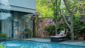 A pool area with a stone wall, a lounge chair, and a person relaxing by the pool. - The Out House Pushkar (Pushkar)