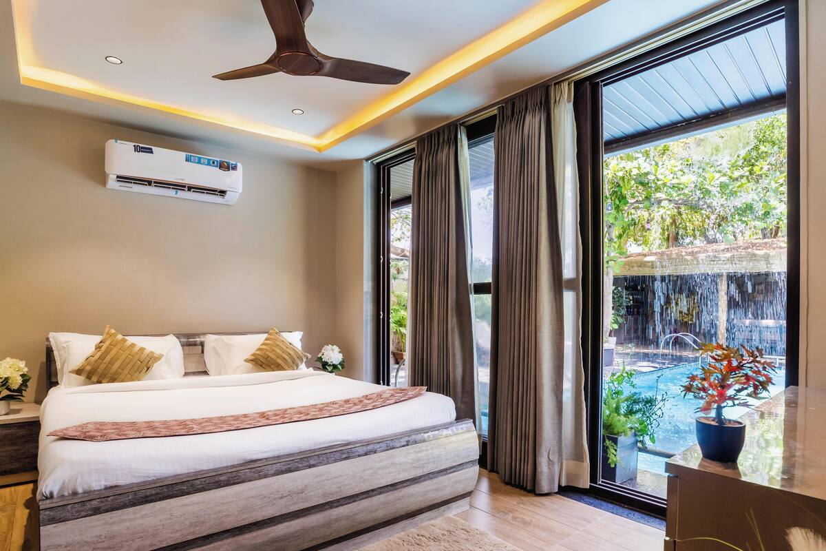 Un dormitorio con una cama grande, un equipo de aire acondicionado, un ventilador de techo y vistas a una cascada.