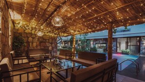 An outdoor seating area with stone walls, wooden furniture, and string lights. - The Out House Pushkar (Pushkar)