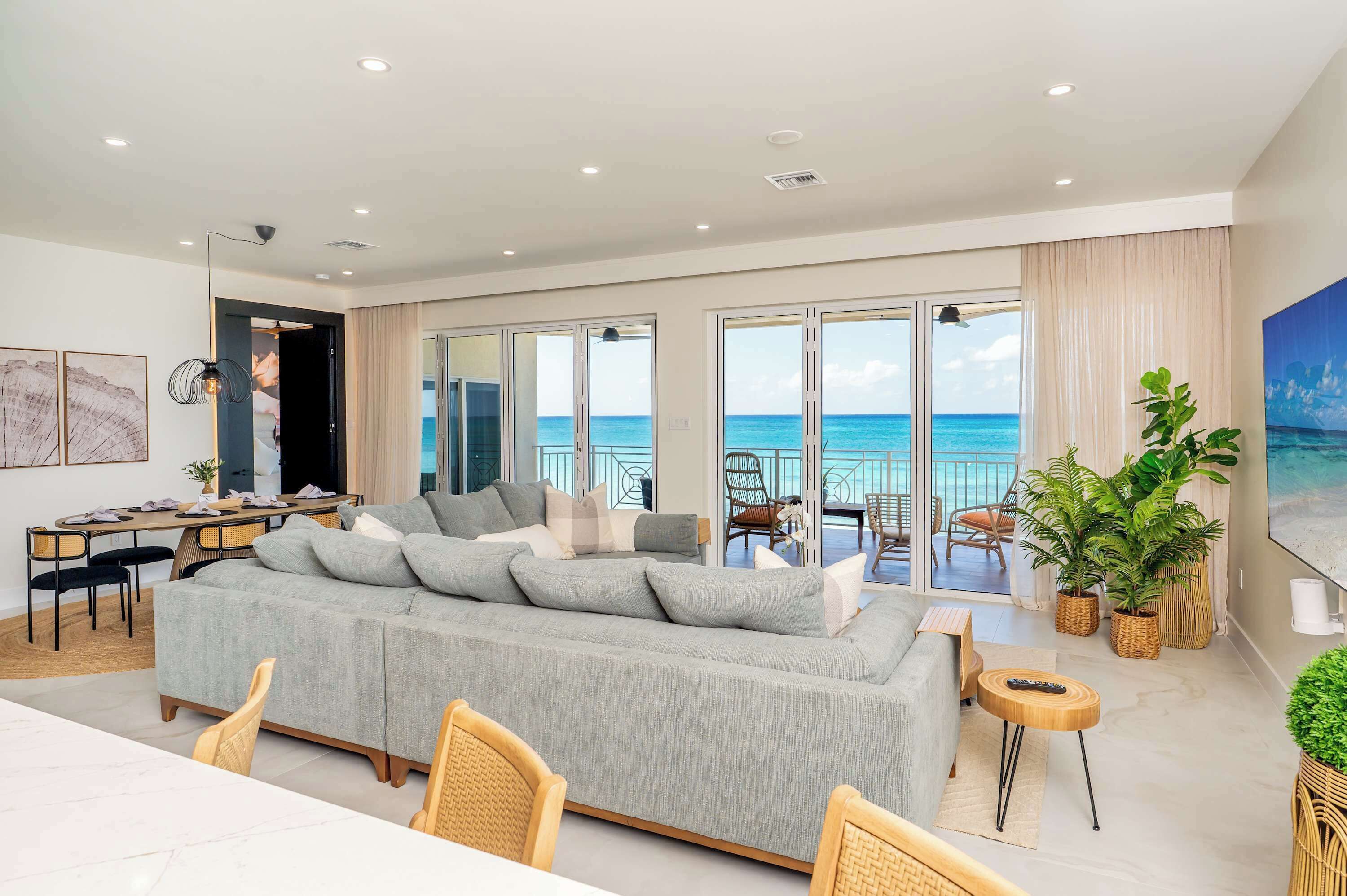 Een moderne woonkamer met een grijze bank, een eethoek en grote ramen met uitzicht op de zee.