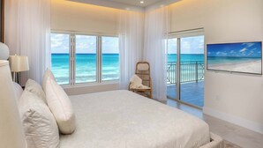 Un dormitorio con una cama grande, una silla, un televisor y vista al océano.
