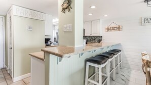 A kitchen with a light blue island, white cabinets, and a 'Paradise' sign. - Beachfront Comfort | 3BR/3BA | 4th Floor | Quiet East End **BEACH CHAIRS (Panama City Beach)