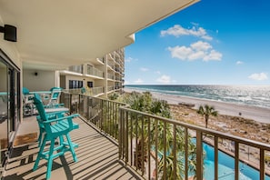 Un balcon avec des chaises turquoise et une piscine donnant sur une plage.