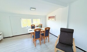 Ruokailutila, jossa on pöytä ja neljä tuolia, ikkuna, jossa on sälekaihtimet, ja yksi tuoli etualalla.