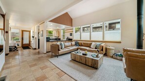 Amplia sala de estar con un sofá seccional grande, una mesa de centro de madera y vistas al exterior a través de amplios ventanales.