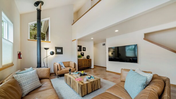 Amplia sala de estar con techo alto, gran ventanal, chimenea, sofá, mesa de centro y televisor.