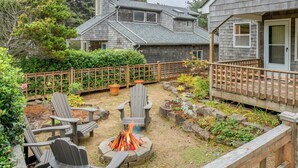 Patio trasero con fogón, sillas Adirondack y terraza de madera.