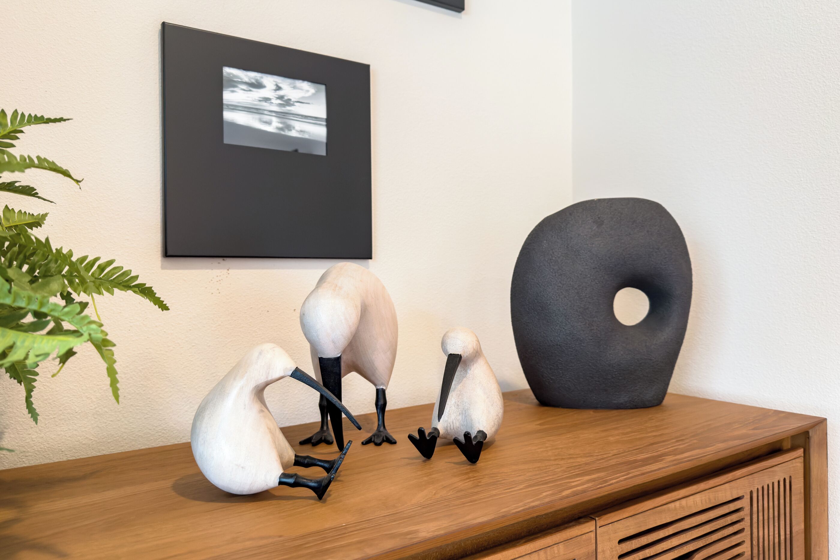Une table en bois sur laquelle sont posées trois sculptures d’oiseaux blanches et une sculpture abstraite noire.