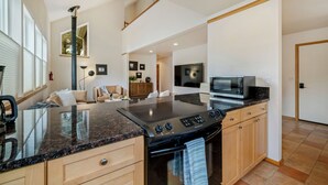Una cocina moderna con una isla grande, horno empotrado y microondas. Hay una zona de comedor con un sofá y una televisión.