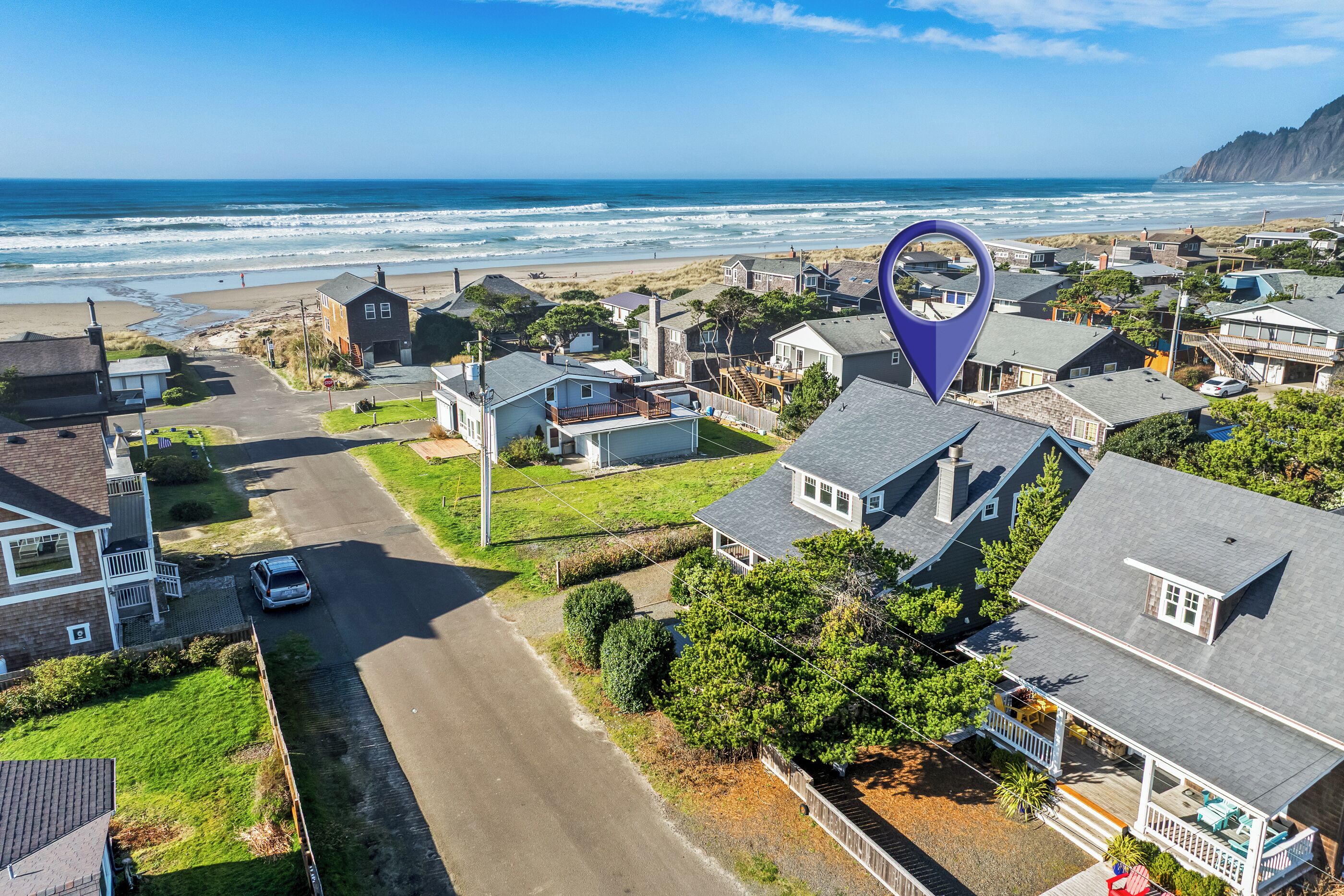 An aerial view of a coastal residential area with houses, a road, and a beach.