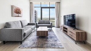 Una sala de estar moderna con un sofá gris, un sillón gris más pequeño, una mesa de centro de madera y un televisor sobre un mueble de madera.