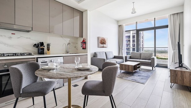 Una sala de estar moderna con una mesa redonda de mármol, sillas tapizadas en gris y un sofá gris.
