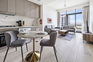 A modern living room with a round marble table, grey upholstered chairs, and a grey sofa. - Cozy 1BR with Balcony Views (Dubai)