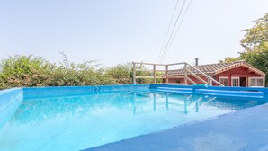 A clear blue swimming pool with a wooden deck and a red building in the background.
