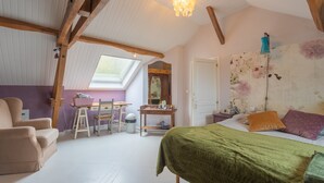 A bedroom with a skylight, a bed with green bedding, a desk with a chair, and a large floral tapestry.