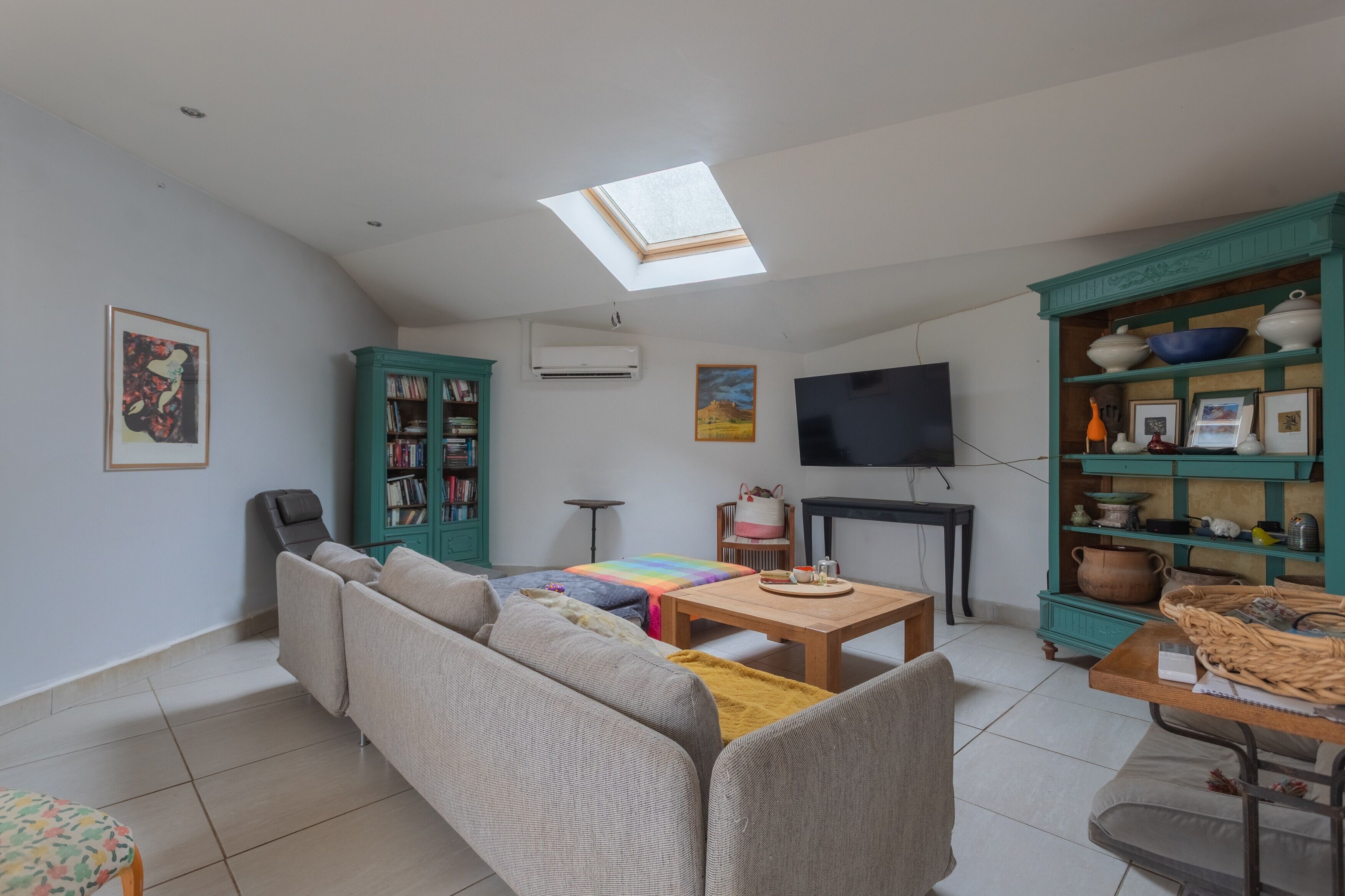 A living room with a sofa, a coffee table, a TV, a bookshelf, and a skylight.