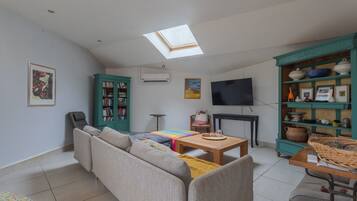 A living room with a sofa, a coffee table, a TV, a bookshelf, and a skylight.