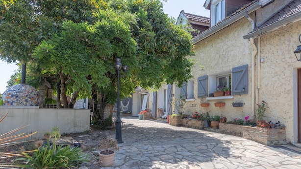 A courtyard with stone flooring, potted plants, and a building with shutters and a tiled roof.