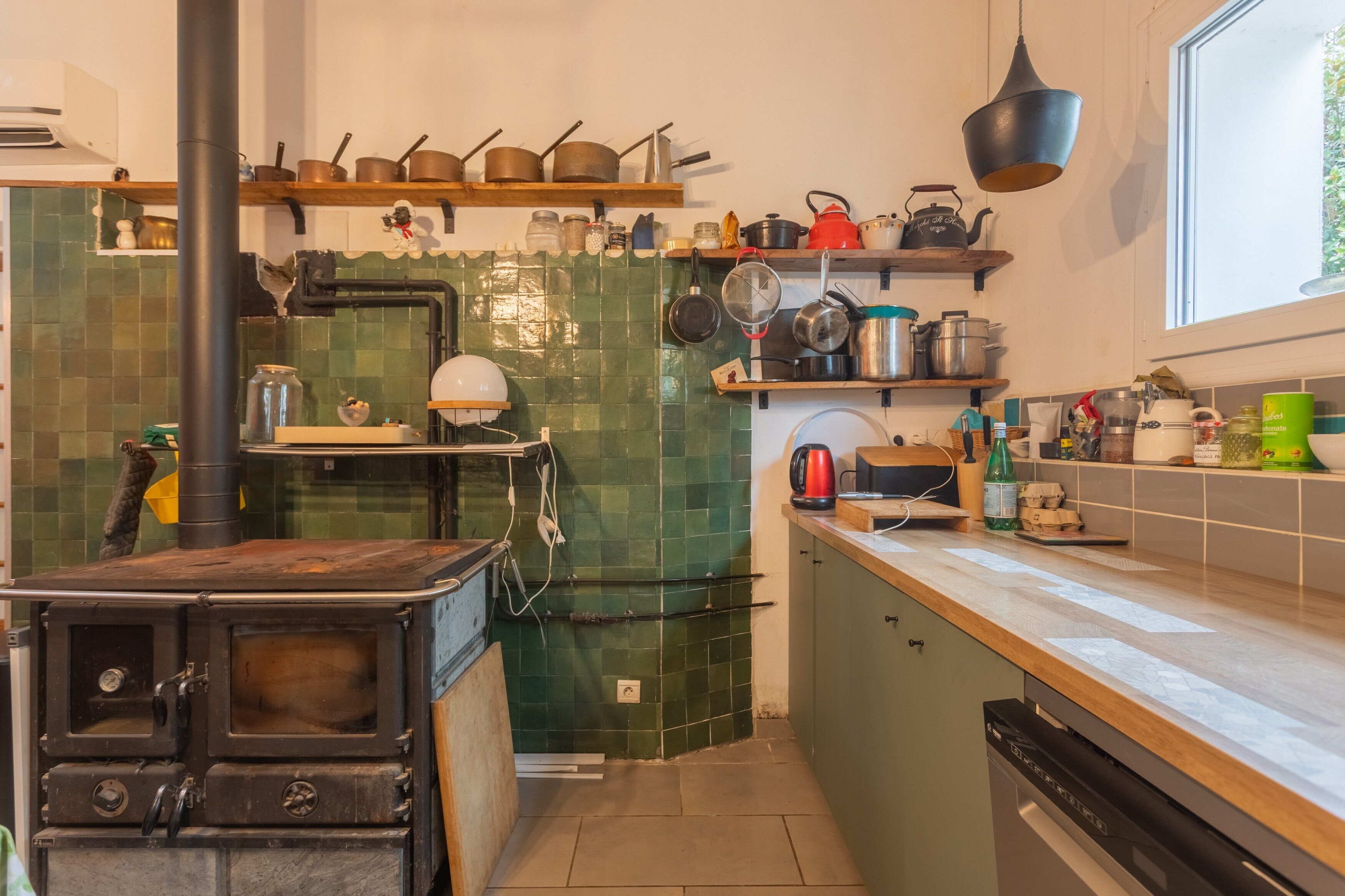 Een keuken met een fornuis, planken met kookgerei en een raam.