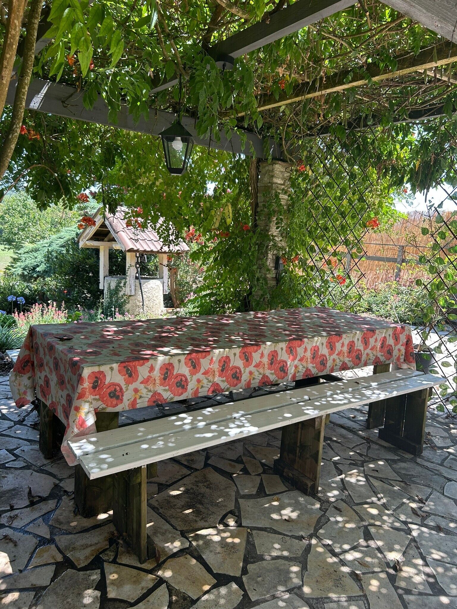 Un espace extérieur abrité, doté d’une table et de bancs, entouré de verdure et recouvert d’un sol en pierres.