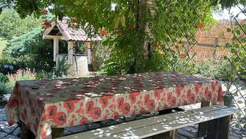 Un espace extérieur abrité, doté d’une table et de bancs, entouré de verdure et recouvert d’un sol en pierres.