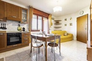 A kitchen with wooden cabinets, a dining table with chairs, a yellow sofa, and a clock on the wall.