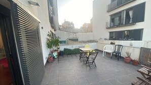 Eine Dachterrasse mit Tisch und Stühlen, Topfpflanzen und Blick auf benachbarte Gebäude.
