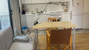 Eine kleine Küche mit weißen Schränken, einem Holztisch und einem Klappstuhl.